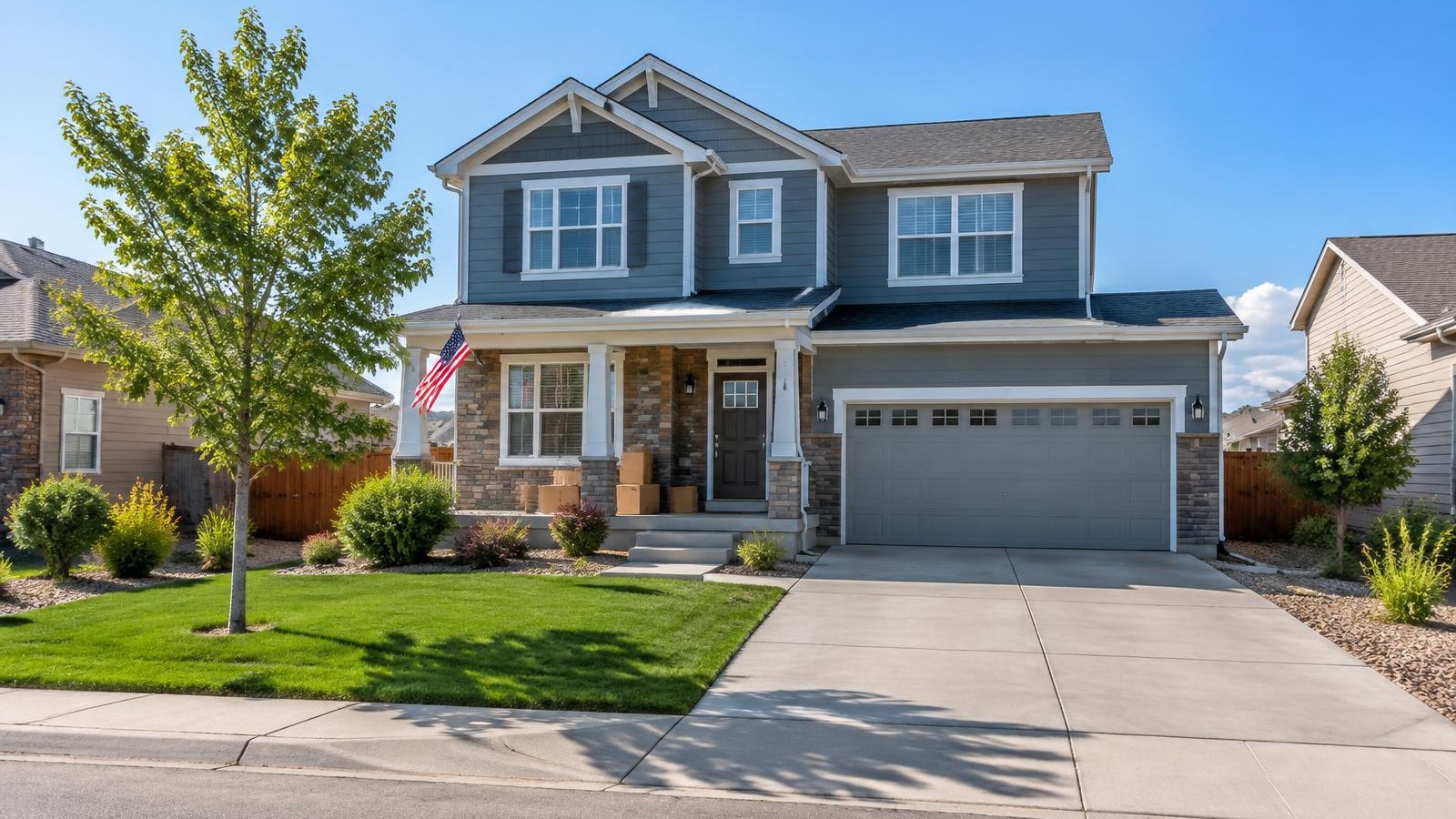 Two-story Aurora home with moving boxes on the front porch and a small American flag in clear September morning light.