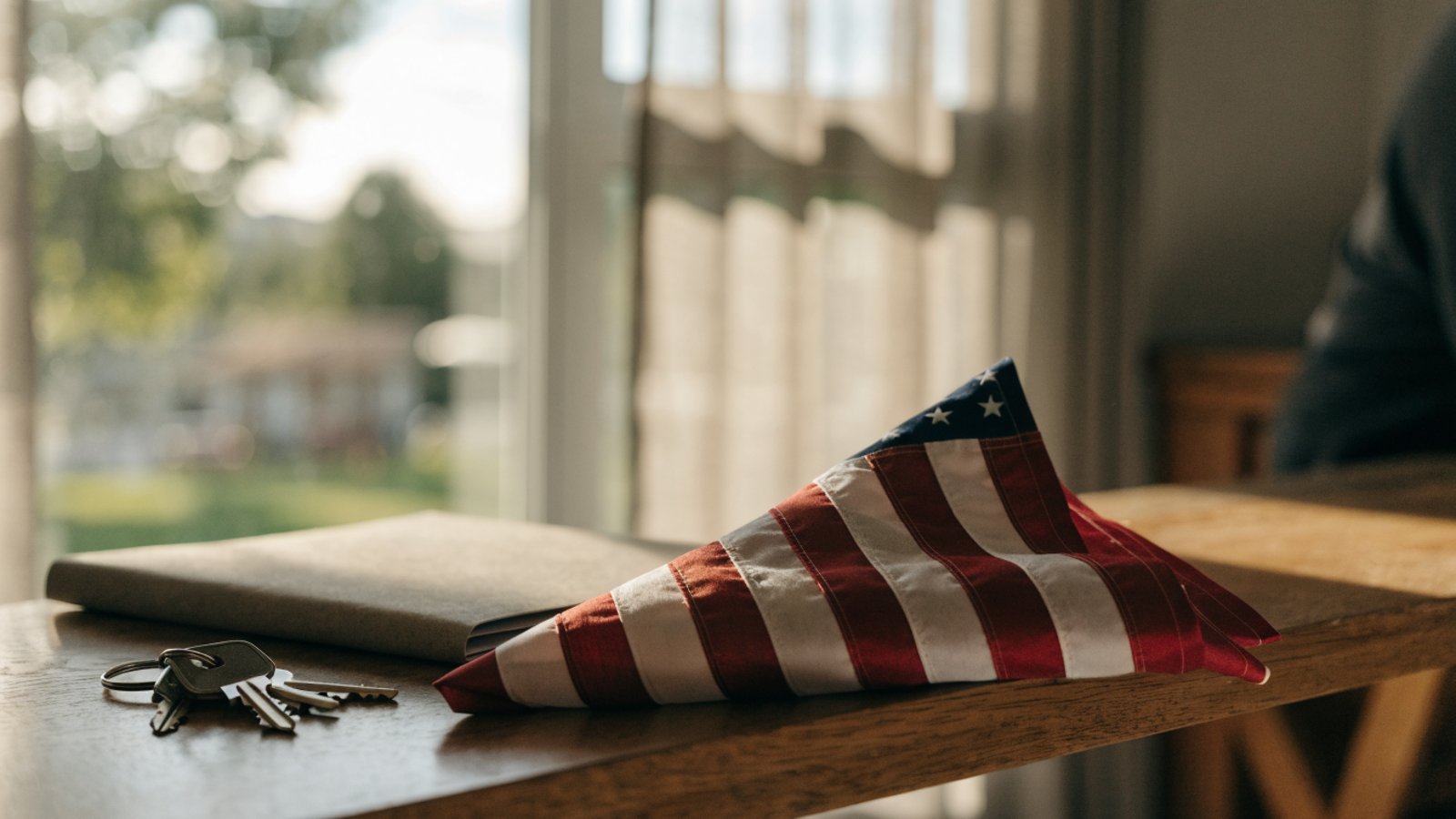 Folded American flag beside house keys and a plain closing folder in soft window light.